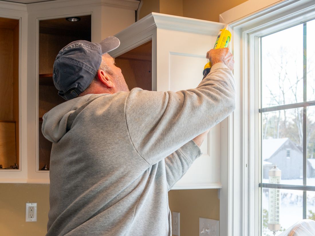 A carpenter finishing trim on new kitchen cabinets